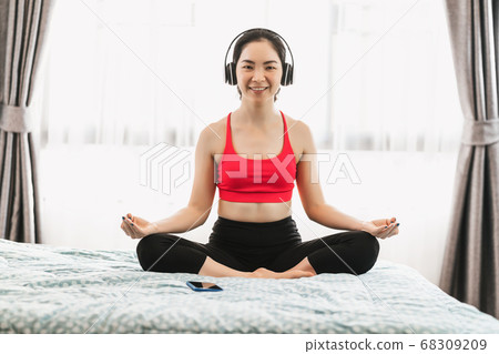 Asian woman practicing yoga from home on bed in bedroom when Covid19 outbreak, healthy or Meditation Exercise, yoga workout at home, coronavirus pandemic and quarantine, sports and healthcare concept Asian woman practicing yoga from home on bed in bedroom when Covid19 outbreak, healthy or Meditation Exercise, yoga workout at home, coronavirus pandemic and quarantine, sports and healthcare concept 68309209