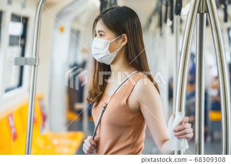 Young Asian woman passenger wearing surgical mask and hand touching with wet wipe in subway train when traveling in big city at Covid19 outbreak, Infection and Pandemic, new normal concept 68309308