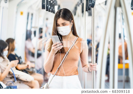 Young Asian woman passenger wearing surgical mask and listening music via smart mobile phone in subway train when traveling in big city at Covid19 outbreak, Infection and Pandemic concept Young Asian woman passenger wearing surgical mask and listening music via smart mobile phone in subway train when traveling in big city at Covid19 outbreak, Infection and Pandemic concept 68309318