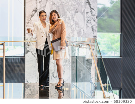 Two asian businesswomen walking and talking during coffee break in modern office or coworking space, coffee break, relaxing and talking after working time, business and people partnership concept Two asian businesswomen walking and talking during coffee break in modern office or coworking space, coffee break, relaxing and talking after working time, business and people partnership concept 68309320