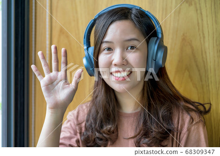 Asian Young woman waving hand for say hello when making video call to friend with social distancing, smiling female taking video blog recording vlog, Covid-19 pandemic, headphone and online meeting 68309347