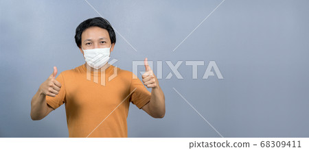 Portrait of asian man wearing face surgical mask with thumbs up like on blue color background, Coronavirus pandemic, covid19 outbreak, social distancing and responsibility, healthcare and protection. Portrait of asian man wearing face surgical mask with thumbs up like on blue color background, Coronavirus pandemic, covid19 outbreak, social distancing and responsibility, healthcare and protection. 68309411