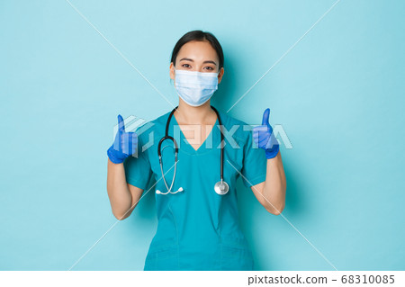 Covid-19, social distancing and coronavirus pandemic concept. Optimistic smiling asian female doctor, physician in medical mask, rubber gloves and scrubs, showing thumbs-up, guarantee quality checkup 68310085