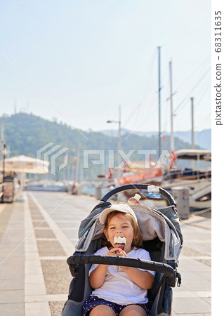 Toddler girl sitting in stroller with ice cream. Traveling with child. Summer trip Toddler girl sitting in stroller with ice cream. Traveling with child. Summer trip 68311635