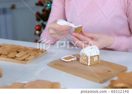 Woman is decorating gingerbread house with sugar sweet icing, hands closeup. Woman is decorating gingerbread house with sugar sweet icing, hands closeup. 68312148