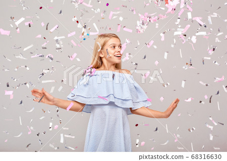 Freestyle. Little girl in dress isolated on gray dancing in flying confetti looking aside smiling surprised Freestyle. Little girl in dress isolated on gray dancing in flying confetti looking aside smiling surprised 68316630