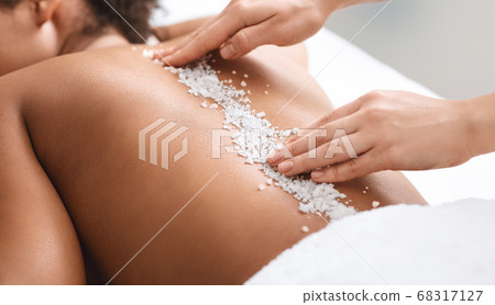 Therapist hands applying sea salt on black female patient spine 68317127