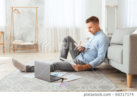 Portrait of man sitting on floor using phone and pc Portrait of man sitting on floor using phone and pc 68317174