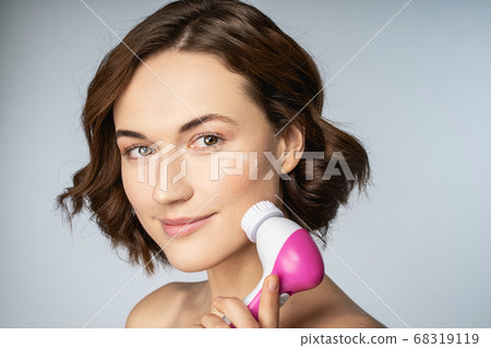 Beautiful young woman using cleansing face brush Beautiful young woman using cleansing face brush 68319119