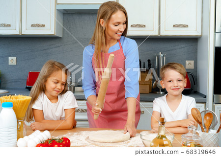 Mother and her little kids, boy and girl, helping her to prepare dough 68319646