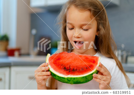 Little girl eating watermelon piece in the kitchen Little girl eating watermelon piece in the kitchen 68319951