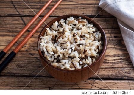 Brown and unpeeled rice on a plate with chopsticks. Wooden rustic background. Copy space. Brown and unpeeled rice on a plate with chopsticks. Wooden rustic background. Copy space. 68320654
