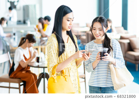 一個年輕的女人，看著一家咖啡館的智能手機 68321800