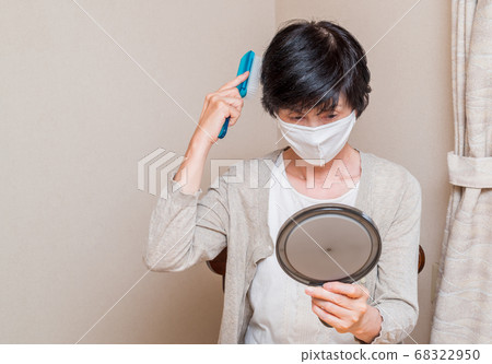 Middle-aged woman wearing a mask looking at a hand mirror Middle-aged woman wearing a mask looking at a hand mirror 68322950