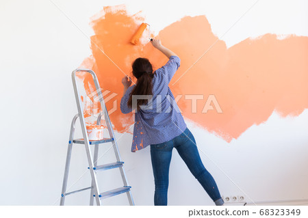 Happy young woman painting wall in her new apartment. Renovation, redecoration and repair concept. 68323349