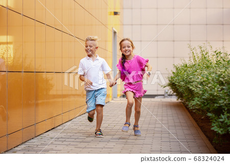 Two smiling kids, boy and girl running together in town, city in summer day 68324024