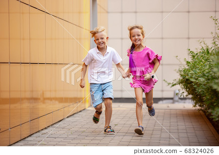 Two smiling kids, boy and girl running together in town, city in summer day 68324026