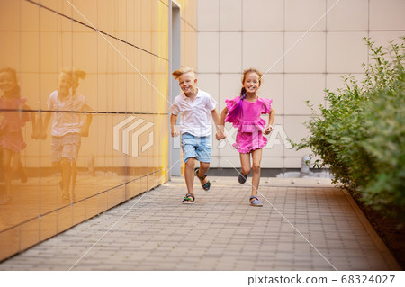 Two smiling kids, boy and girl running together in town, city in summer day 68324027