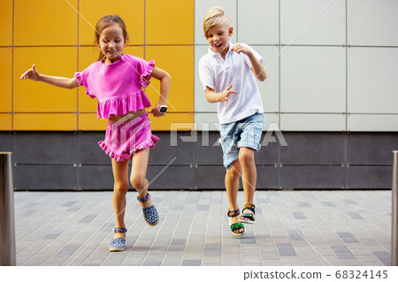 Two smiling kids, boy and girl running together in town, city in summer day 68324145