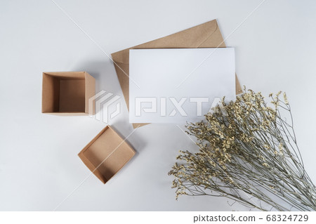 Blank white paper on brown paper envelope with Limonium dry flower and Carton box. Mock-up of horizontal blank greeting card. Top view of Craft paper envelope on white background. Flat lay minimalism 68324729