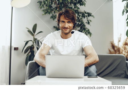 Young man businessman with headset working on laptop from home 68325659