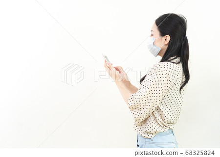 Woman with smartphone wearing mask 68325824