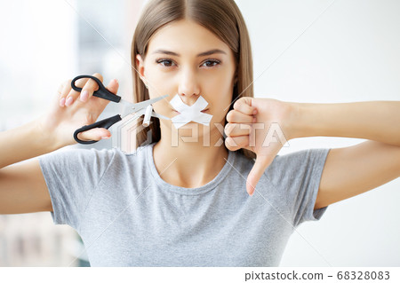 Stop smoking, a woman with a sealed mouth cuts a cigarette with scissors 68328083