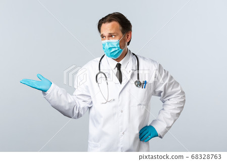 Covid-19, preventing virus, healthcare workers and vaccination concept. Skeptical disappointed doctor in medical mask and gloves, pointing and staring at something bad, white background 68328763