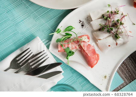 Ham on a plate in the center and cutlery nearby 68328764