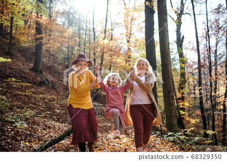 Small girl with mother and grandmother on a walk in autumn forest. 68329350