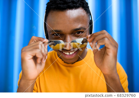 Young black man with sunglasses standing against blue background, black lives matter concept. Young black man with sunglasses standing against blue background, black lives matter concept. 68329760