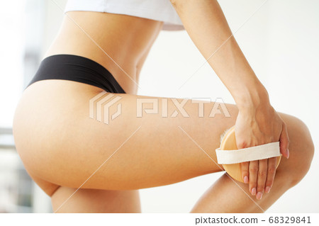 Woman arm holding dry brush to top of her leg, cellulite treatment and dry brushing. Woman arm holding dry brush to top of her leg, cellulite treatment and dry brushing. 68329841