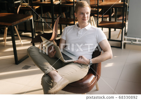 Smiling young businessman wearing fashion casual clothing sitting on chair and holding laptop. 68330892