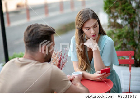 Couple having misunderstanding in open air cafe, female looking down at her phone 68331688