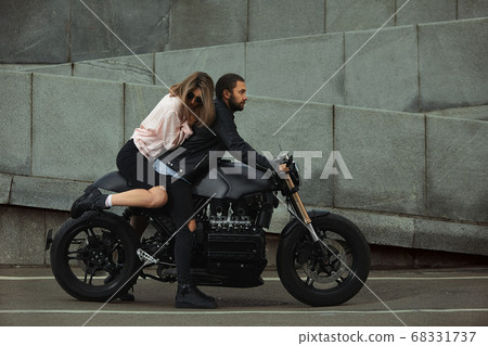 fashion couple sitting on a motorcycle, stone wall on the background. young man and woman with modern motorcycle 68331737