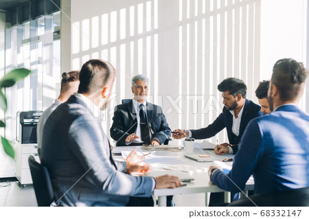 Multiracial male business executives discuss project sitting at conference table Multiracial male business executives discuss project sitting at conference table 68332147