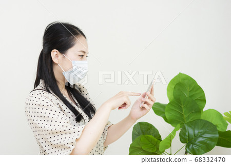 A woman wearing a mask and operating a smartphone A woman wearing a mask and operating a smartphone 68332470