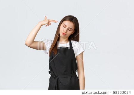 Grocery store employees, small business and coffee shops concept. Annoyed and tired saleswoman in black apron pointing fake gun at head irritated, staring skeptical and bothered Grocery store employees, small business and coffee shops concept. Annoyed and tired saleswoman in black apron pointing fake gun at head irritated, staring skeptical and bothered 68333054