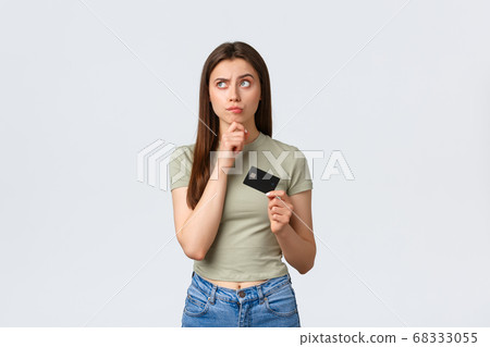 Shopping mall, lifestyle and fashion concept. Thoughtful pleased woman thinking what buy for money on bank account, looking left with pleased smile and holding credit card Shopping mall, lifestyle and fashion concept. Thoughtful pleased woman thinking what buy for money on bank account, looking left with pleased smile and holding credit card 68333055