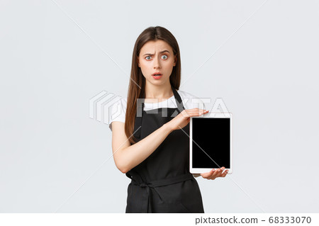 Grocery store employees, small business and coffee shops concept. Confused and puzzled cute girl barista in black apron raise eyebrow shocked and showing digital tablet screen Grocery store employees, small business and coffee shops concept. Confused and puzzled cute girl barista in black apron raise eyebrow shocked and showing digital tablet screen 68333070
