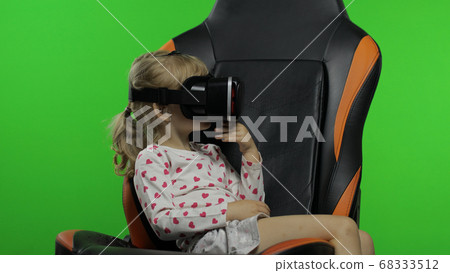 Child girl using VR helmet to play simulation game app. Watch virtual reality 3d video. Chroma key 68333512