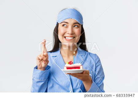 Celebration, lifestyle and holiday concept. Hopeful and dreamy smiling happy asian woman in sleeping mask and pajama, congratulated with birthday in bed, making wish before blowing candle on cake 68333947