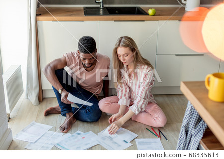 African young man and european woman with long hair looking at papers in kitchen African young man and european woman with long hair looking at papers in kitchen 68335613
