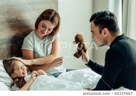 joyful father and mother with ill daughter on bed 68335687
