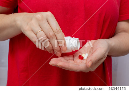 a woman in a red t-shirt holds a bottle of pills and pours medicine in her palm a woman in a red t-shirt holds a bottle of pills and pours medicine in her palm 68344153