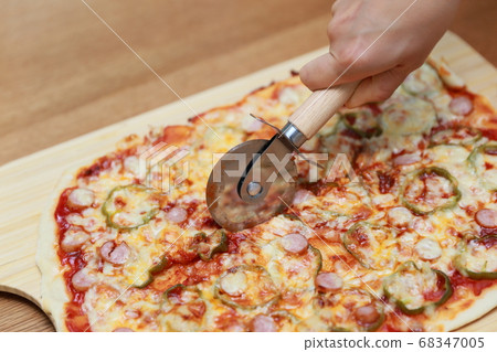 Housewife cutting homemade pizza with a cutter at home Housewife cutting homemade pizza with a cutter at home 68347005