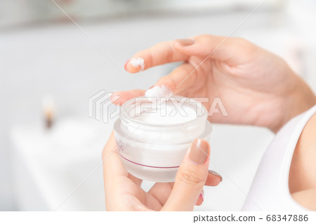 A woman holds a moisturizer in her hand and her A woman holds a moisturizer in her hand and her 68347886