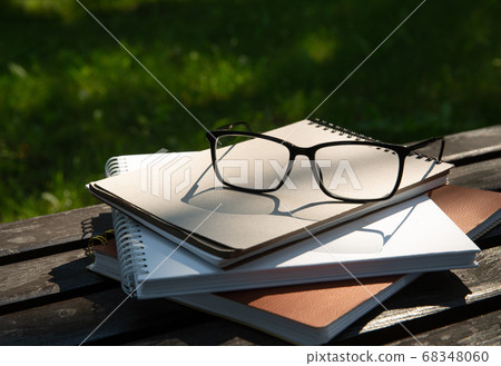 glasses lie on top of a pile of books with a notebook on a bench in the park glasses lie on top of a pile of books with a notebook on a bench in the park 68348060