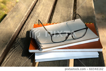 glasses lie on top of a pile of books with a notebook on a bench in the park glasses lie on top of a pile of books with a notebook on a bench in the park 68348182