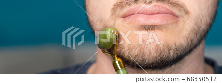Bearded man is using jade face roller 68350512